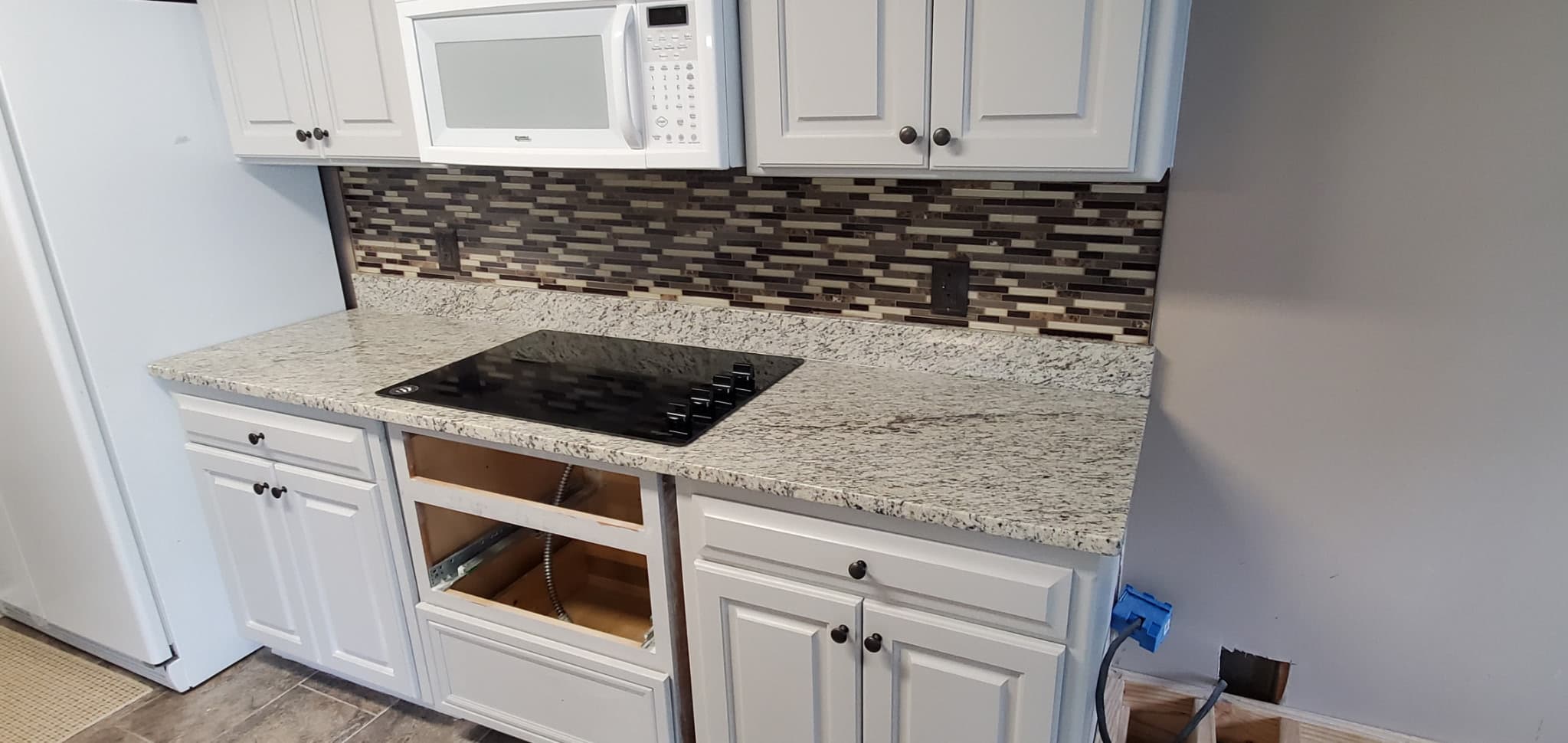 White speckled granite counters with cooktop and mosaic backsplash